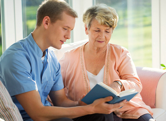 Male caregiver reading with elderly woman.