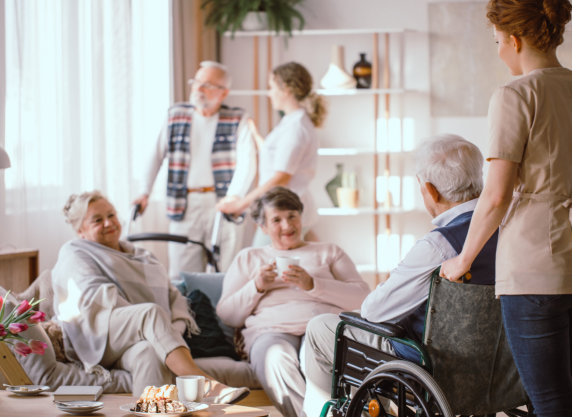 Female nurse with man in wheelchair looking at other elderly people.