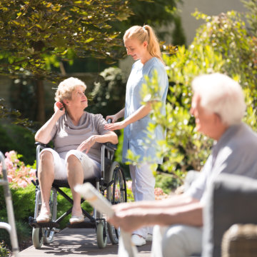 Woman in wheelchair with her nurse outside.