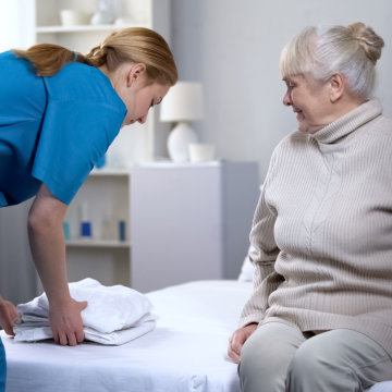 Caregiver preparing bed-linen to elderly woman.