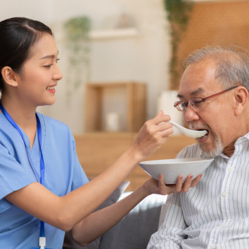 Nurse feeding breakfast to man.