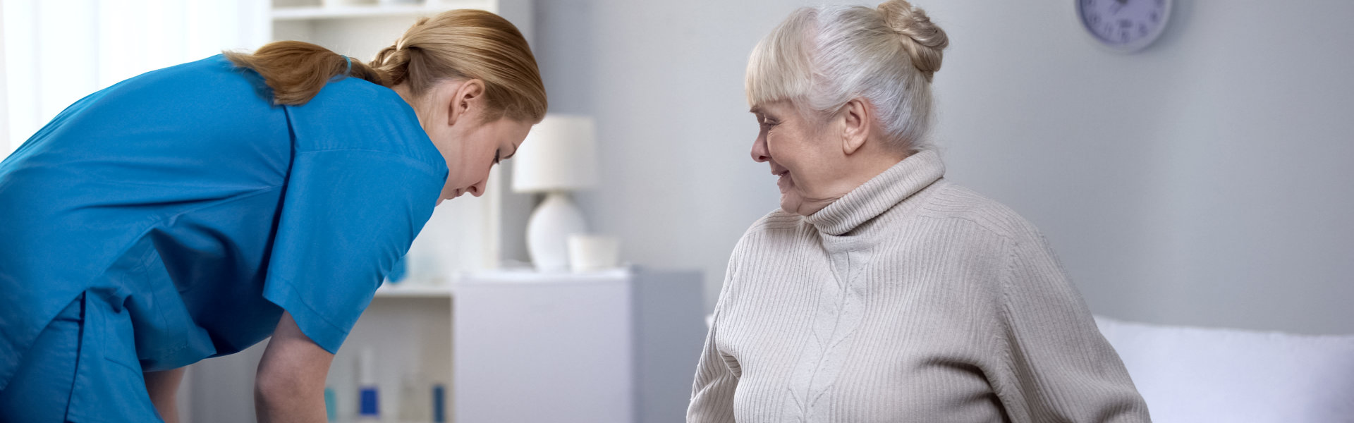 Caregiver preparing bed-linen to elderly woman.